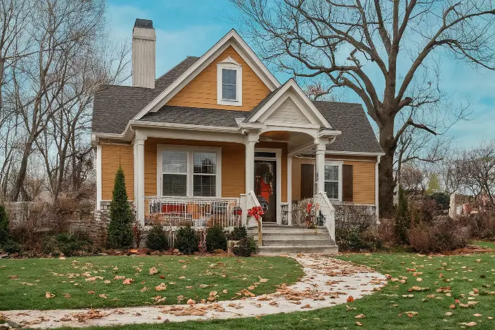 A cozy two-story home painted orange and surrounded by trees during autumn. Winter tree care is important for trees’ overall health.